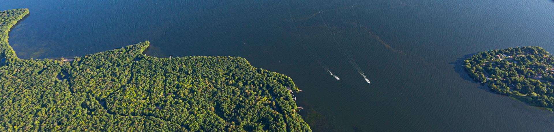 Aerial view of huge Lake Mille Lacs with 2 boats driving between two green points of land.