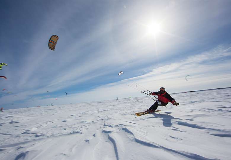 Man on large, frozen, snow-covered Lake Mille Lacs being pulled by airborne, colorful wind-surfing kite.